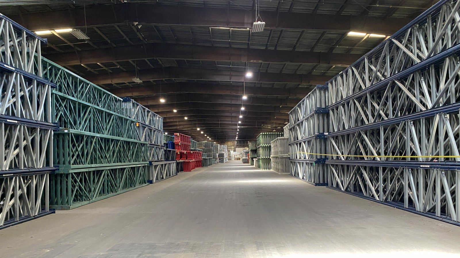 A long aisle of AMH's owned rack inventory: stacked upright frames in green, galvanized, and red, ready to ship