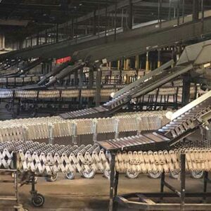 A large industrial facility features an extensive network of gravity conveyors. The foreground shows a series of flexible, accordion-like conveyor sections on wheels, designed for easy maneuverability and adjustment. Overhead, additional conveyor belts are visible, creating a multi-level system for efficient material handling. The facility has a high ceiling with visible structural supports and industrial lighting, emphasizing its scale and capacity for high-volume sorting and distribution operations. The overall scene highlights a well-coordinated, automated process essential for large-scale logistics and warehousing.