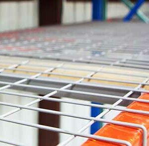 Close-up view of a metal wire mesh decking on an industrial shelving unit. The wire mesh is supported by orange beams, providing a sturdy and organized surface for storage. The background is slightly blurred, focusing attention on the details of the wire mesh and the orange support beams. The overall setting appears to be within a warehouse or storage facility.